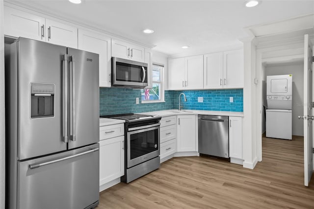 kitchen with stainless steel appliances, light hardwood / wood-style floors, white cabinetry, stacked washer / drying machine, and crown molding