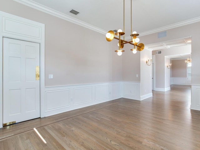 spare room featuring an inviting chandelier, ornamental molding, and light hardwood / wood-style floors