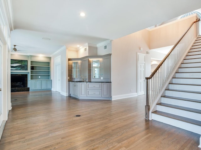 unfurnished living room with sink, built in features, ceiling fan, crown molding, and hardwood / wood-style flooring