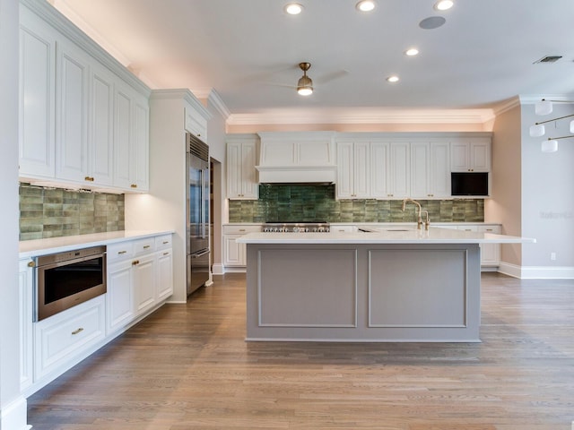 kitchen featuring crown molding, stainless steel appliances, backsplash, and a kitchen island with sink