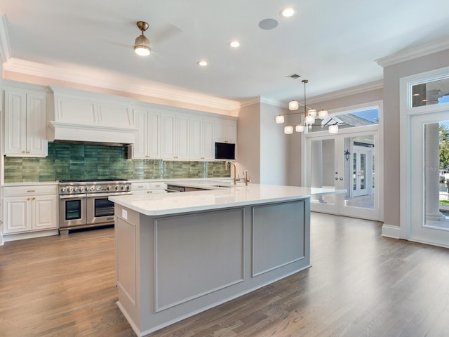 kitchen with tasteful backsplash, decorative light fixtures, white cabinets, custom range hood, and double oven range