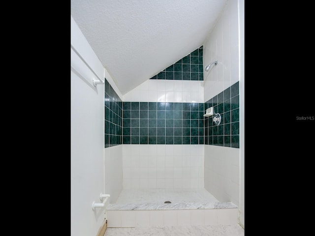 bathroom featuring a textured ceiling, vaulted ceiling, and tiled shower