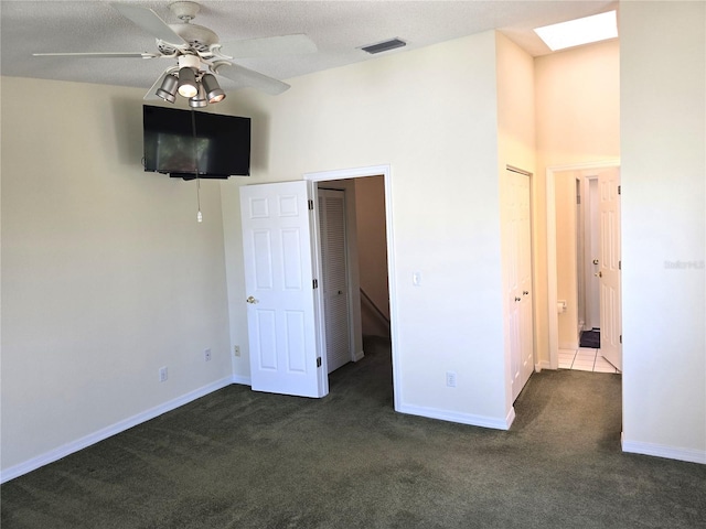 unfurnished bedroom with a closet, a textured ceiling, dark colored carpet, ceiling fan, and a skylight