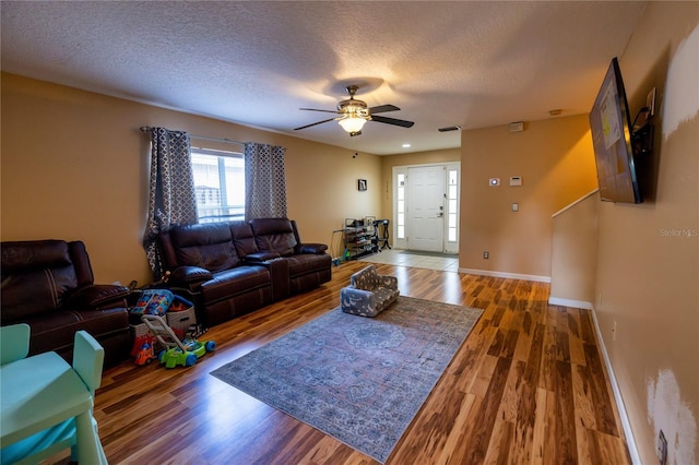 living room with ceiling fan, a textured ceiling, and dark wood-type flooring