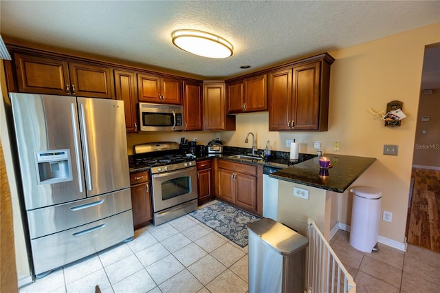 kitchen with light tile patterned flooring, stainless steel appliances, a textured ceiling, dark stone counters, and sink