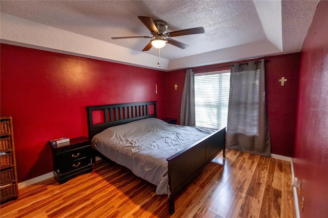 bedroom with a textured ceiling, a raised ceiling, hardwood / wood-style floors, and ceiling fan