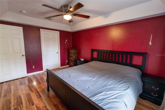 bedroom with wood-type flooring, ceiling fan, a raised ceiling, and a textured ceiling