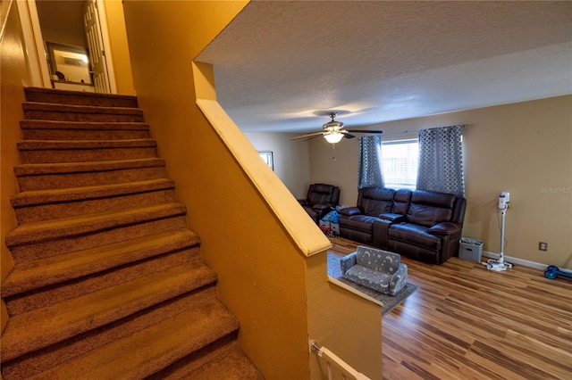 stairway with ceiling fan, hardwood / wood-style flooring, and a textured ceiling