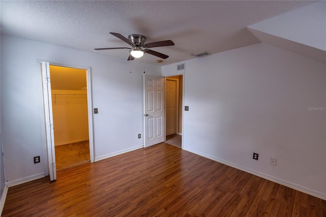 unfurnished bedroom with dark hardwood / wood-style flooring, a closet, a textured ceiling, ceiling fan, and a walk in closet