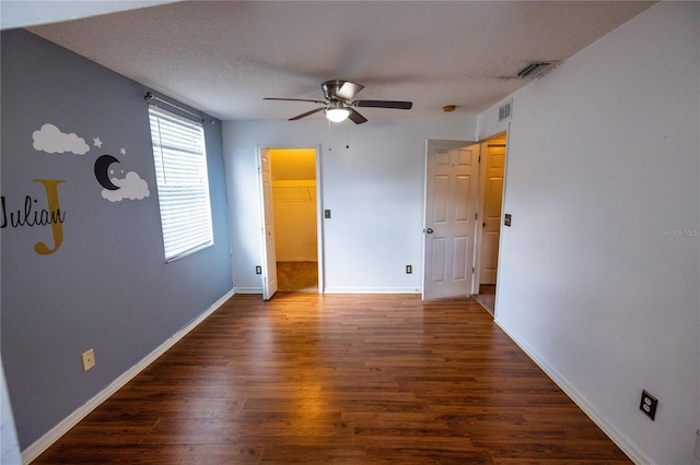 unfurnished bedroom featuring a textured ceiling, dark hardwood / wood-style flooring, ceiling fan, and a walk in closet