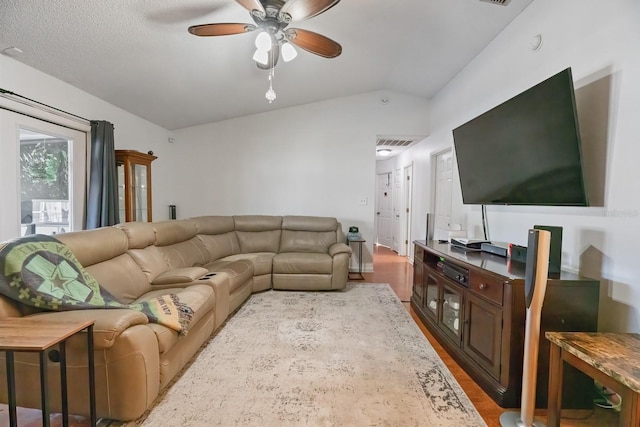 living room with light wood-type flooring, vaulted ceiling, ceiling fan, and a textured ceiling