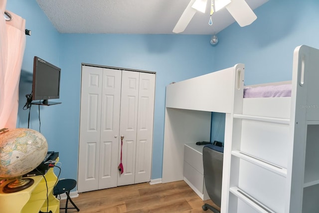 bedroom with light hardwood / wood-style floors, vaulted ceiling, a closet, a textured ceiling, and ceiling fan