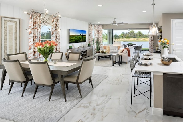 dining room with ceiling fan with notable chandelier, wooden walls, and sink