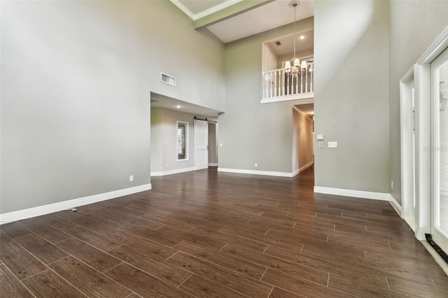 unfurnished living room featuring a towering ceiling, a barn door, and a chandelier