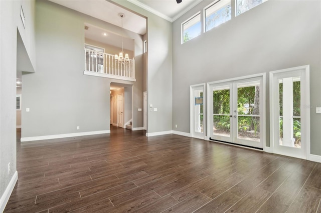 unfurnished living room featuring french doors, a towering ceiling, crown molding, and a notable chandelier