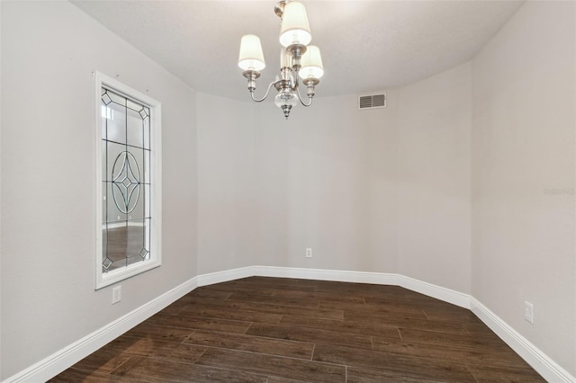 empty room with dark hardwood / wood-style flooring and an inviting chandelier