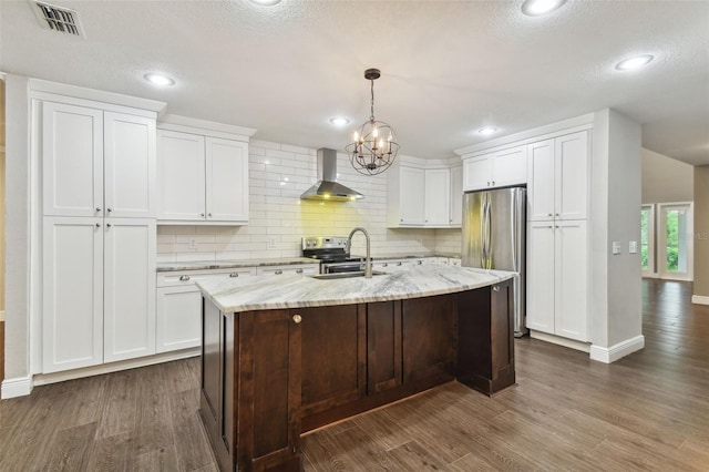 kitchen featuring sink, wall chimney range hood, an island with sink, stainless steel appliances, and white cabinets