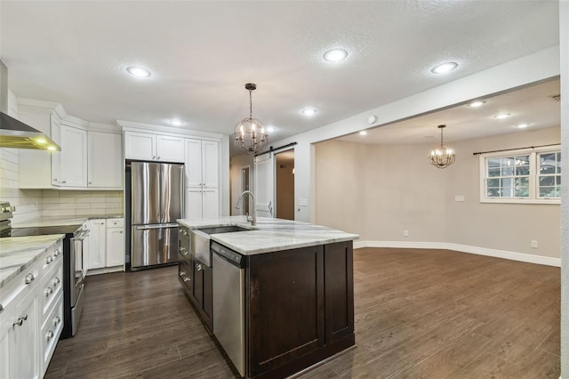 kitchen with appliances with stainless steel finishes, pendant lighting, white cabinetry, an island with sink, and decorative backsplash