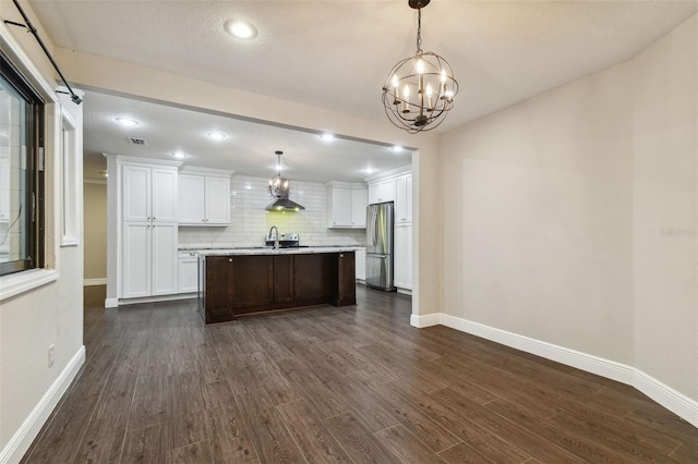 kitchen with hanging light fixtures, stainless steel fridge, white cabinets, and a center island with sink