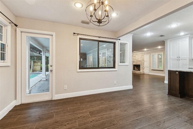 unfurnished dining area with a stone fireplace, dark hardwood / wood-style floors, and a chandelier