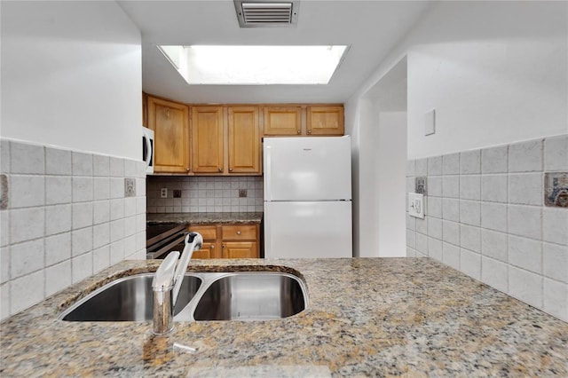 kitchen with a skylight, light stone countertops, sink, and white appliances