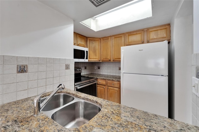 kitchen with light stone counters, backsplash, sink, and white appliances