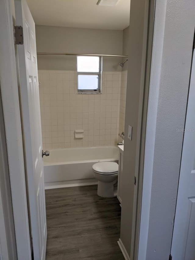 bathroom with wood-type flooring, tiled shower / bath, and toilet