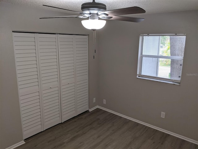 unfurnished bedroom with ceiling fan, a textured ceiling, a closet, and dark hardwood / wood-style floors