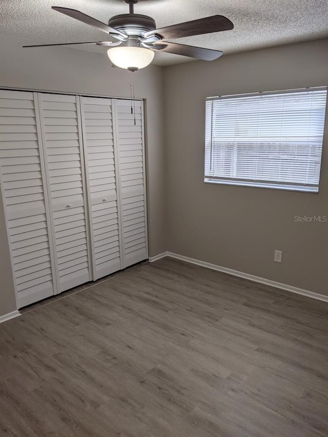 unfurnished bedroom featuring ceiling fan, a textured ceiling, a closet, and wood-type flooring