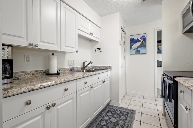 kitchen with white cabinets, sink, a textured ceiling, light tile patterned flooring, and stainless steel appliances