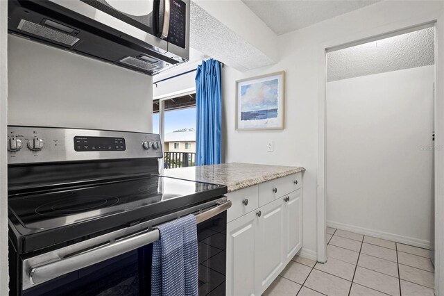 kitchen with a textured ceiling, stainless steel appliances, white cabinetry, and light tile patterned flooring