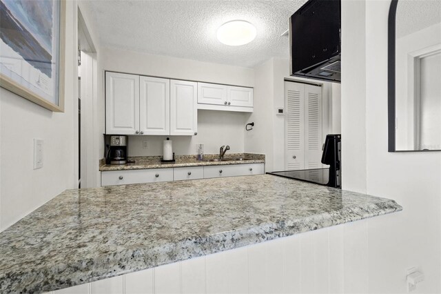 kitchen featuring a textured ceiling, light stone counters, white cabinetry, and sink