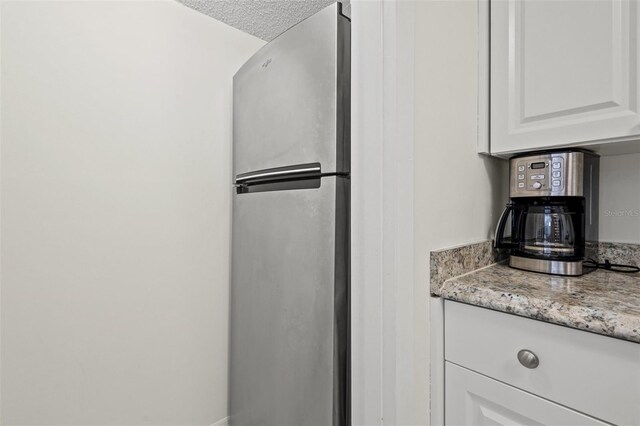 kitchen featuring white cabinetry, stainless steel fridge, light stone countertops, and a textured ceiling