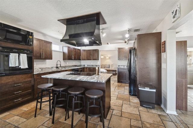 kitchen with a textured ceiling, a center island, a kitchen breakfast bar, black appliances, and exhaust hood