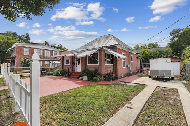 bungalow featuring brick siding, a patio, entry steps, a front yard, and fence