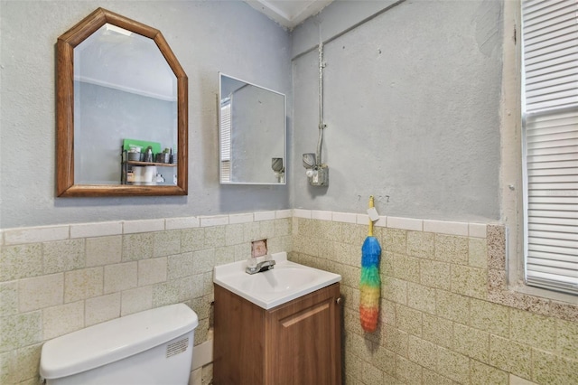 half bath with a wainscoted wall, vanity, toilet, and tile walls