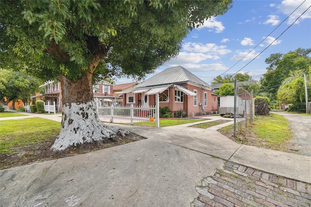 view of front of house featuring metal roof, brick siding, fence, driveway, and a front yard