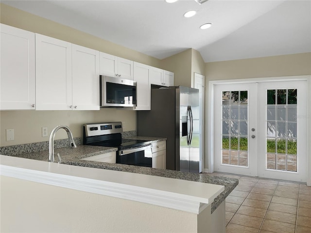 kitchen featuring white cabinets, vaulted ceiling, kitchen peninsula, stainless steel appliances, and light tile patterned floors