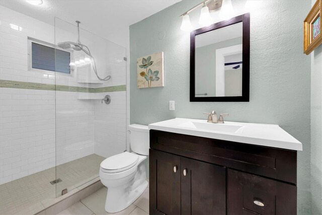 bathroom with tile patterned flooring, tiled shower, vanity, and toilet