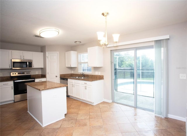 kitchen with appliances with stainless steel finishes, hanging light fixtures, white cabinetry, a center island, and a notable chandelier