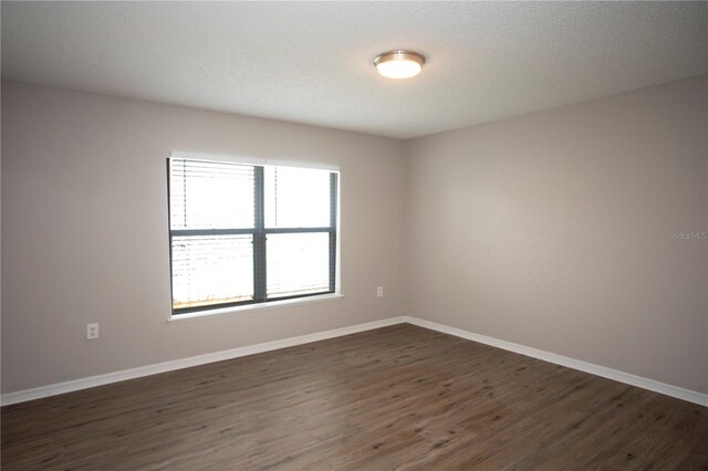 spare room with dark wood-type flooring, baseboards, and a textured ceiling
