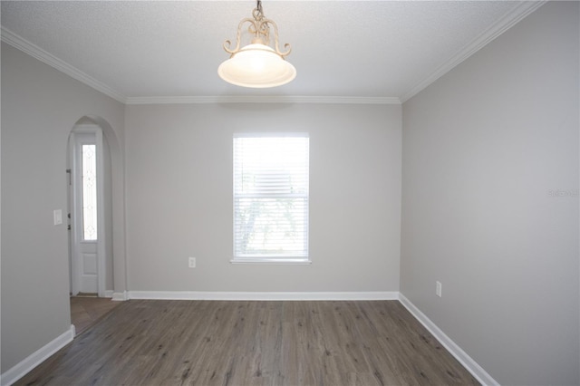 empty room featuring arched walkways, crown molding, baseboards, and wood finished floors