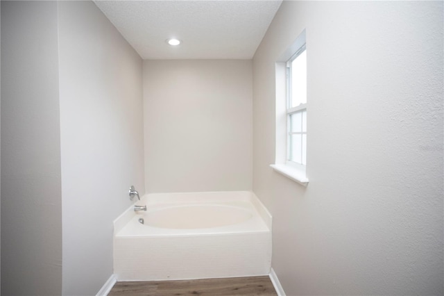 full bath with baseboards, a garden tub, and wood finished floors