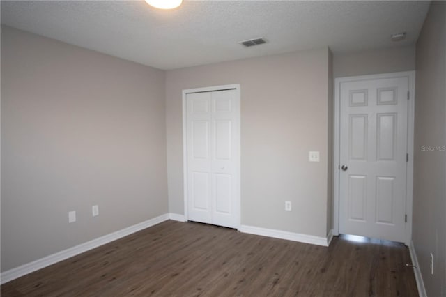 unfurnished bedroom with a textured ceiling, dark wood-type flooring, and a closet