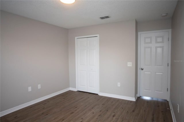unfurnished bedroom with visible vents, dark wood-type flooring, baseboards, a closet, and a textured ceiling