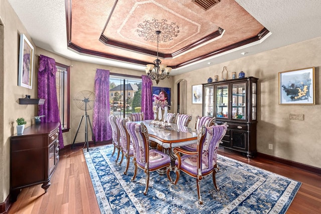 dining space with a textured ceiling, wood-type flooring, crown molding, a tray ceiling, and a chandelier