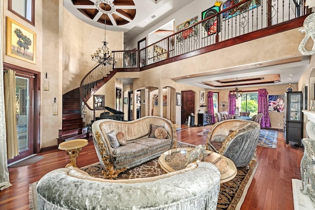 living room with ceiling fan with notable chandelier, dark wood-type flooring, a raised ceiling, and a high ceiling