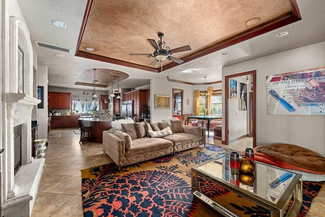 tiled living room featuring ceiling fan with notable chandelier, a textured ceiling, a tray ceiling, and crown molding