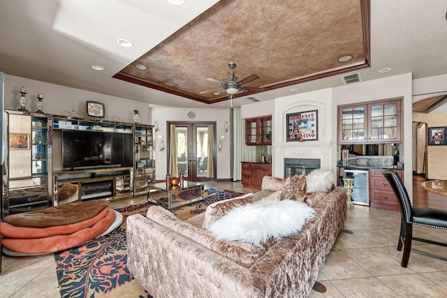 tiled living room with a raised ceiling, a textured ceiling, beverage cooler, ceiling fan, and french doors