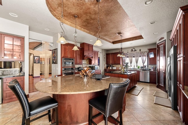 kitchen featuring a tray ceiling, a textured ceiling, a center island, hanging light fixtures, and stainless steel appliances